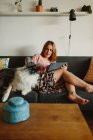 Positif femme pieds nus avec tablette souriant et caressant mignon Collie tout en étant assis sur un canapé confortable à la maison — Photo de stock