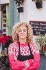 Позитивна доросла жінка з схрещеними руками посміхається і дивиться на камеру, стоячи біля входу в місцевий продовольчий магазин — стокове фото