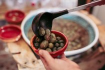 Personne méconnaissable mettant une louche d'olives dans un bol tout en travaillant dans un magasin d'aliments local — Photo de stock