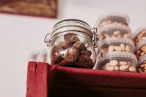 From below glass jar with truffles and plastic boxes with pistachios placed on red wooden shelf in local delicatessen food store — Stock Photo