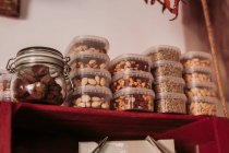 Bocal en verre avec truffes et boîtes en plastique avec pistaches placées sur une étagère en bois rouge dans un épicerie fine locale — Photo de stock
