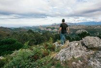 Back view of faceless male in casual outfit standing on edge of cliff and enjoying amazing scenery of mountain range against cloudy sky in Alicante in Spain — Stock Photo