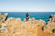 Jeune femme assise sur une falaise près de la mer — Photo de stock