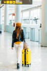 Teenager in modischem Outfit mit Gepäck und Reisepass in der Gesäßtasche blickt in die Kamera und winkt zum Abschied, während er neben dem Check-in-Schalter am Flughafen steht — Stockfoto