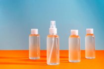 Varios frascos transparentes con gel clorhídrico para desinfectar las manos de covid-19 sobre fondo azul y naranja - foto de stock