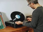 Seitenansicht eines ernsten Mannes, der Plattenspieler aufstellt und Songs auf Retro-Vinyl genießt, während er zu Hause chillt — Stockfoto