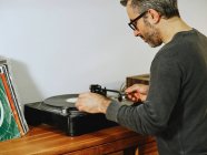 Side view of serious man setting turntable and enjoying songs on retro vinyl disc while chilling at home — Stock Photo