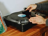 Zugeschnittene unkenntliche Person, die Plattenspieler aufstellt und Songs auf Retro-Vinyl-Disc genießt, während sie zu Hause chillt — Stockfoto