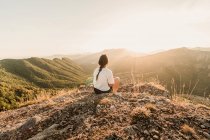 Rückansicht einer anonymen Touristin in Freizeitkleidung, die an einem sonnigen Sommertag die malerische Landschaft genießt, während sie auf steinigem Boden sitzt — Stockfoto