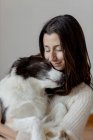 Заботливая женщина в шерстяном свитере обнимает смешную собаку Пограничного Колли, сидя вместе на деревянном полу — стоковое фото