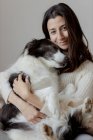 Fürsorgliche Hündin im Wollpullover umarmt lustigen Border Collie Hund, während sie gemeinsam auf dem Holzboden sitzt und in die Kamera schaut — Stockfoto