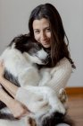 Cura femminile in maglione di lana abbracciare divertente Border Collie cane mentre seduti sul pavimento di legno insieme guardando la fotocamera — Foto stock