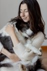 Cuidando a la hembra en suéter de lana abrazando al divertido perro Border Collie mientras están sentados juntos en el suelo de madera - foto de stock