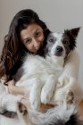 Заботливая женщина в шерстяном свитере, обнимающая смешную пограничную собаку Колли, сидящую на деревянном полу и смотрящую в камеру — стоковое фото