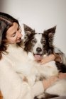 Fürsorgliche Hündin im Wollpullover umarmt lustigen Border Collie Hund, während sie gemeinsam auf Holzboden sitzt — Stockfoto