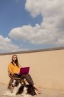 Жінка в повсякденному одязі сидить на стілець і переглядає фіолетовий ноутбук під час роботи і насолоджується сонцем на терасі будинку під час карантину. — стокове фото