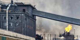 Edificios industriales deteriorados y tuberías que emiten humo y llamas en la fábrica de coque - foto de stock