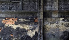 Pared de ladrillo grueso con yeso sucio desmoronado ubicado dentro de una antigua instalación industrial abandonada - foto de stock