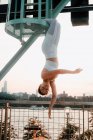 Низкий угол спокойная женщина в спортивной одежде висит вверх ногами с закрытыми глазами во время медитации на фоне городского пейзажа — стоковое фото