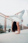 Low angle side view of flexible woman in sports bra and leggings performing scorpion handstand while exercising barefoot and leaning on metal railing in city — Stock Photo