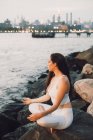 Зверху зору концентрованої жінки в активному одязі, що сидить на камені на набережній під час практики йоги — стокове фото