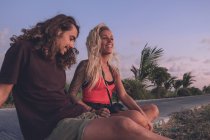 Conteúdo casal de hipsters viajando sentado à beira da estrada à noite e assistindo ao pôr do sol enquanto relaxa e olha para longe — Fotografia de Stock