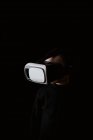Enfant portant un pull noir et expérimentant un casque VR tout en se tenant contre un mur noir — Photo de stock