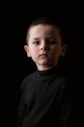 Retrato de menino pensativo olhando para a câmera durante a tomada de estúdio tiro contra fundo preto — Fotografia de Stock
