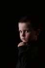 Porträt eines nachdenklichen kleinen Jungen, der während der Studioaufnahme vor schwarzem Hintergrund in die Kamera blickt — Stockfoto