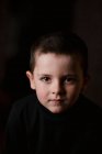 Retrato de menino pensativo olhando para a câmera durante a tomada de estúdio tiro contra fundo preto — Fotografia de Stock