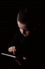 Adorable serious child in casual wear holding tablet in hands with determined look isolated on black background — Stock Photo