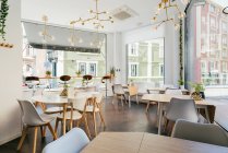 Interieur des geräumigen, hellen modernen Restaurants mit großen Fenstern mit exotischen Pflanzen und gemütlichen Stühlen an Tischen unter kreativen Pendellampen — Stockfoto