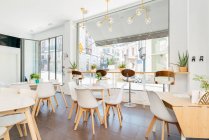 Інтер'єр просторого світлого сучасного ресторану з великими вікнами, прикрашеними екзотичними рослинами і затишними стільцями за столами під творчими підвісними лампами — стокове фото