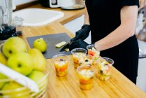 Кукурудза жінка в чорному фартусі і рукавички, які рубають свіжі зелені яблука ножем і готують здорові свіжі десерти на сучасній кухні — стокове фото