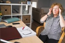 Seitenansicht einer fokussierten erwachsenen Frau in lässiger Kleidung, die Musik in Kopfhörern mit geschlossenen Augen genießt, während sie während der Arbeit an Laptop und Notebook ruht — Stockfoto