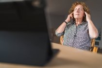 Side view of focused adult woman in casual clothes enjoying music in earphones with closed eyes while resting during work on laptop and notebook — Stock Photo