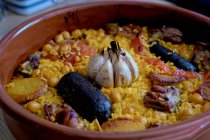 Clay casserole with delicious dish made of baked rice and chickpeas with vegetables and blood sausages garnished with head of garlic — Stock Photo