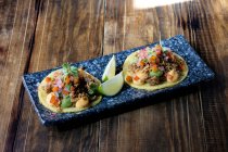 Hohe Winkel der köstlichen Taco aus Maistortilla und Fleisch mit gehacktem frischem Gemüse und Soßen garniert, während auf dem Teller mit Limettenkeilen serviert — Stockfoto