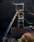 Дезертирований старий високий іржавий металевий шахтний механізм, розташований на тлі розмитого темного лісу в сільській місцевості в сонячний осінній день — стокове фото