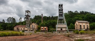 Empty yard with old abandoned buildings and mine mechanisms locating against cloudy sky and green trees on gloomy day in countryside — Stock Photo