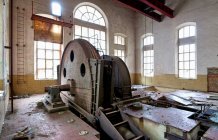 Industrial circular machine with metal mechanism locating inside deserted ownerless dilapidated industrial workshop with light walls and large arched windows — Stock Photo