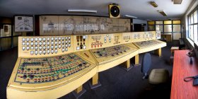 Vieux tableaux de bord jaunes avec de nombreux boutons capteurs et cadrans dans la salle de contrôle avec des dessins et des diagrammes sur le mur dans la construction déserte de la mine de charbon négligence — Photo de stock