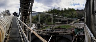 Старі нежитлові промислові будівлі з візками для транспортування вугілля в сільській місцевості з видом на зелені гори на покинутій вугільній шахті в похмурий день — стокове фото