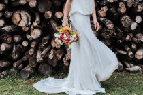 Unrecognizable lady in white dress and with bridal bouquet spinning around while dancing near stacks of log during wedding in countryside — Stock Photo