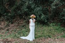 Счастливая невеста покрывает лицо рядом с кустом — стоковое фото