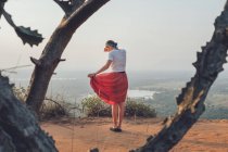 Vista posterior de la mujer en camiseta casual y falda de pie en la colina de arena y cubriendo la cara mientras disfruta de la puesta de sol y viajar por Sri Lanka - foto de stock