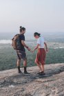 From above side view of couple of hipsters in casual wear holding hands and enjoying sunset on stone edge of hill while traveling around Sigiriya in Sri Lanka — Stock Photo
