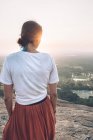 Back view of unrecognizable traveling woman in casual clothes and bandana admiring scenic landscape during vacation in Sigiriya while standing in back lit and looking away — Stock Photo