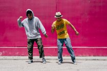Двоє молодих чоловіків танцюють біля рожевої стіни на вулиці — стокове фото