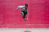 Junge hispanische Männer springen in der Nähe einer rosa Mauer auf der Straße — Stockfoto
